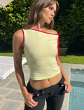 Wearing the TIGERMIST ALIRA TOP in yellow, a woman stands by a pool outdoors on a sunny day with greenery behind her, one hand on her hip.