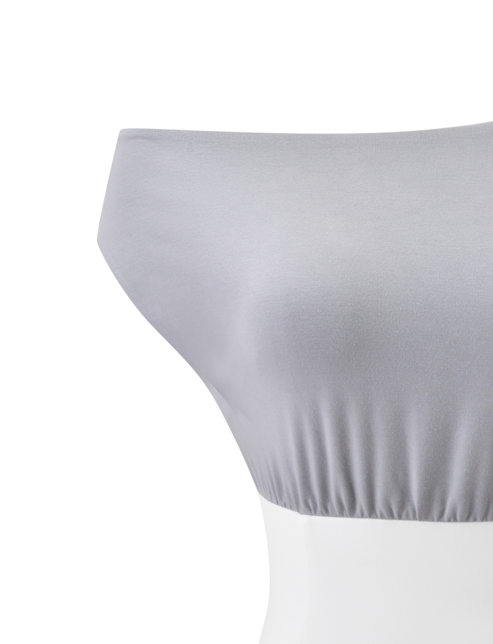 The ALYSSA OFF SHOULDER TOP - GREY by TIGERMIST features a smooth light gray finish, subtle hem ruching, and hints of a corseted waist, showcased on a white mannequin against a plain white background.