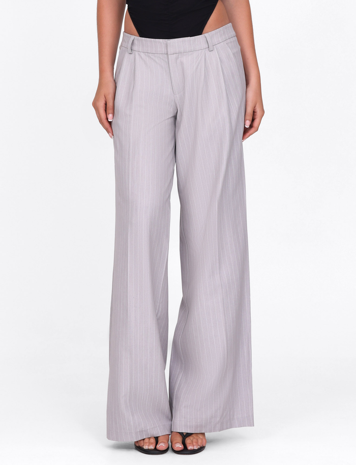 A person wears the TIGERMIST AMBERLY SUIT PANT in grey pinstripe, tailored from high-quality suiting fabric, paired with black open-toe heels, against a plain white background.