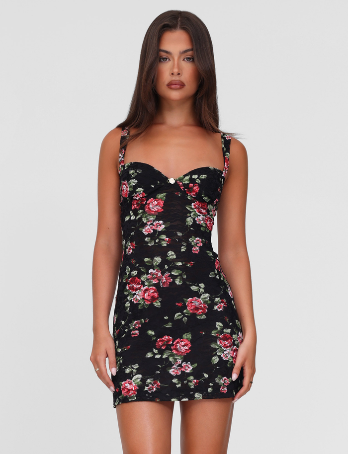 A woman with long brown hair wears the TIGERMIST ANDEE MINI DRESS in BlackRose—a fitted black dress with red and pink floral prints—standing against a plain white background.