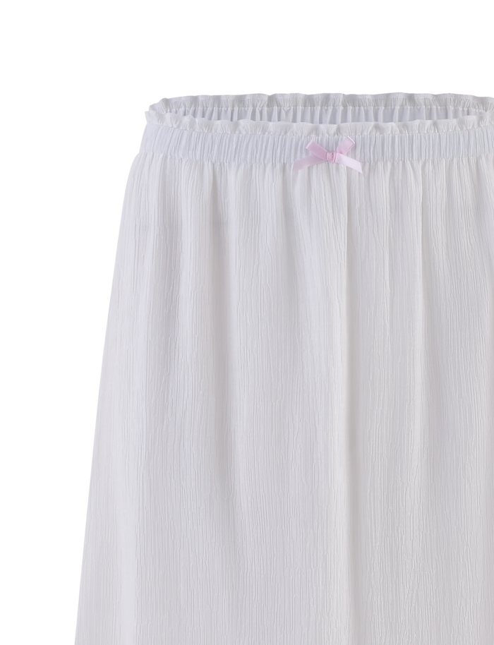 A close-up of the TIGERMIST ASHLYNN MAXI SKIRT in white, featuring textured fabric, an elastic waist, and a small satin bow trim at the center.