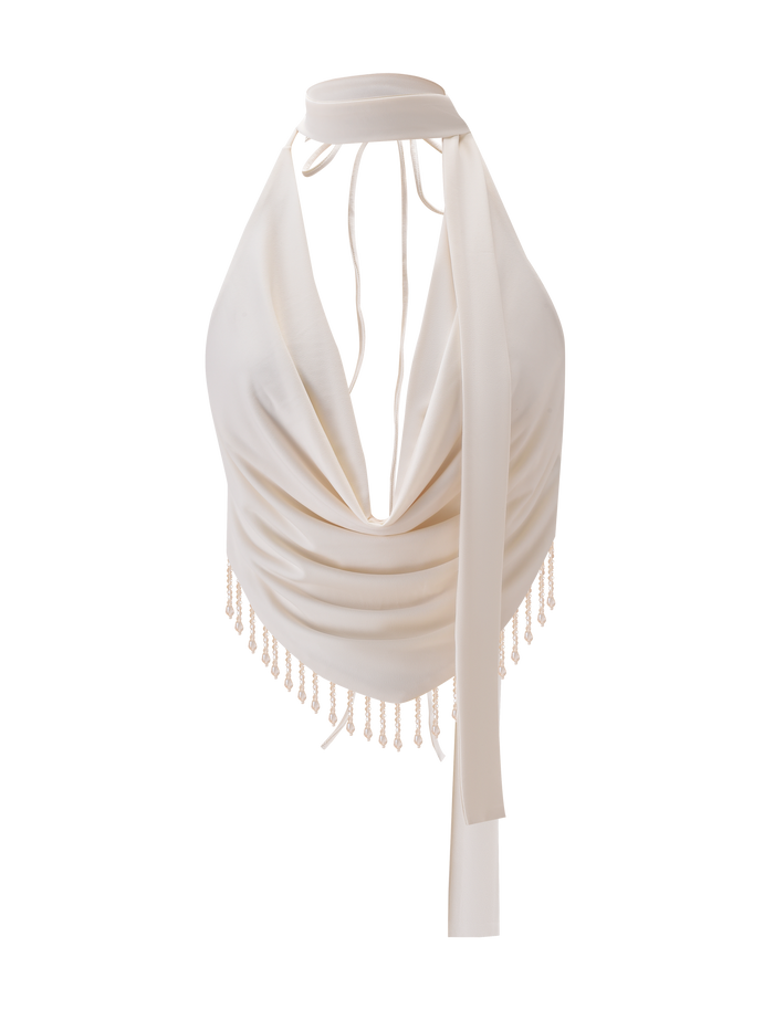 The AUBRIELLA TASSLE TOP by TIGERMIST features a cream cowl halter neck, long ties, open back, and beaded fringe on a handkerchief hem, shown against a plain white background.