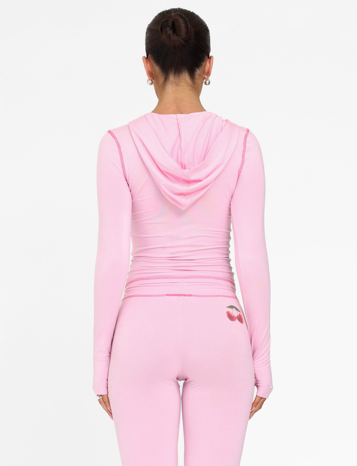 A dark-haired woman in a bun wears the TIGERMIST BLAYZE HOODIE - PINK : SOFT PINK and matching leggings with a cherry graphic, facing away against a plain white background.