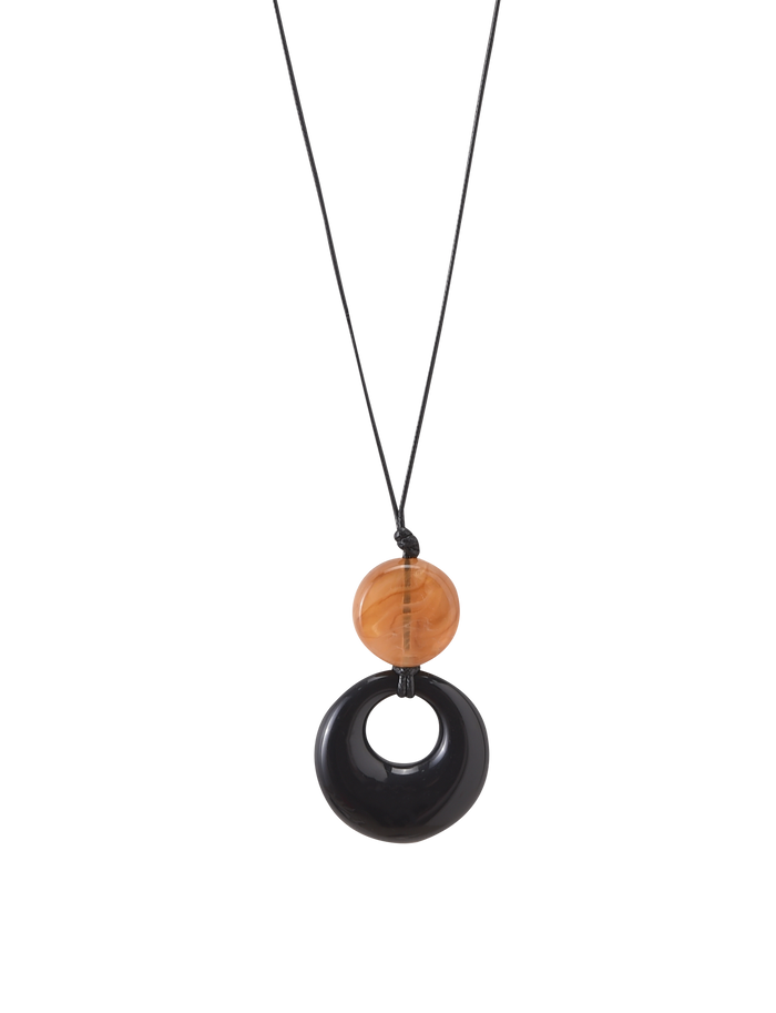 The TIGERMIST BREYA PENDANT NECKLACE - TAN features a minimalist black cord with a round, translucent tortoiseshell bead and a larger glossy black resin pendant with an open center.