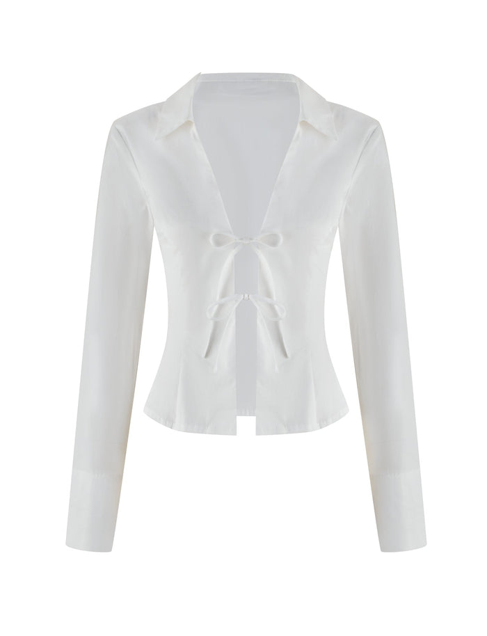 The BRIELLE SHIRT - WHITE by TIGERMIST is a white long-sleeve blouse with a deep V-neck and two front bow ties, offering a minimalistic, elegant design. Its soft stretch fabric is smooth, slightly glossy against the plain white background, and features a classic collar to accentuate its sophisticated charm.