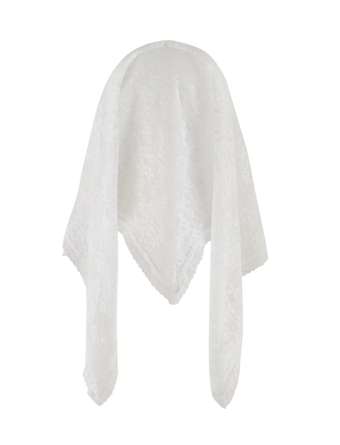 A woman with long dark hair stands against a plain background, wearing a strapless white lace top and a brown mini skirt with ruffled detailing. She has her hands by her sides, adorned with the BRIONY SCARF - WHITE by TIGERMIST, and is looking directly at the camera.
