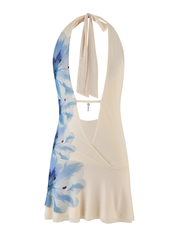 The BROOKS DRESS by TIGERMIST is a cream, sleeveless halter dress with a blue floral print, open back with neck tie, wrap-style front, plunging neckline, and subtle ruffled hem.