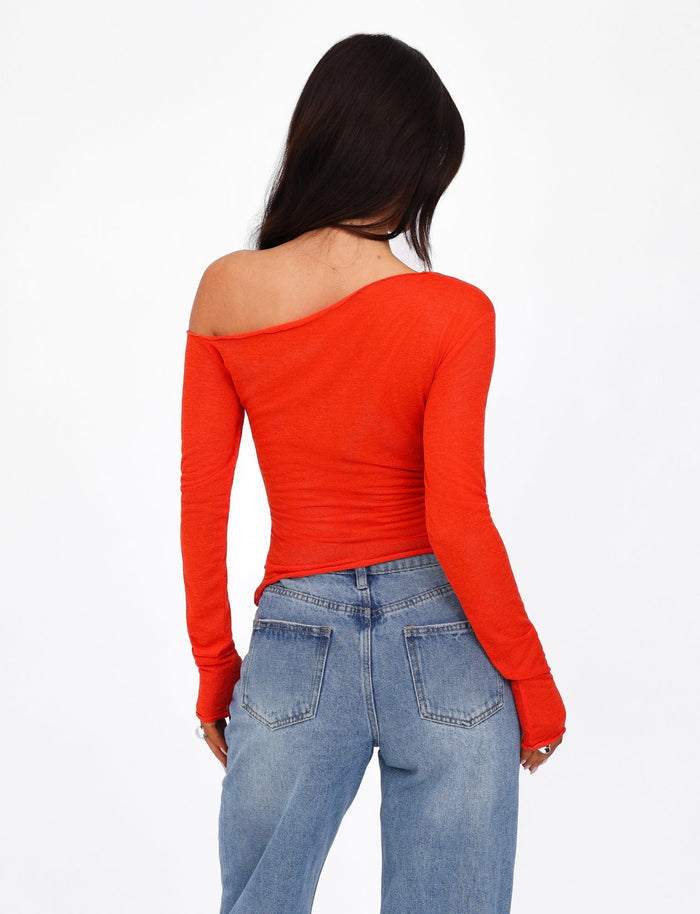 A person with long dark hair, facing away from the camera, wears a long-sleeved, off-the-shoulder BRYNA JUMPER in red by TIGERMIST paired with blue jeans. The knit fabrication of the outfit showcases a casual and stylish look. The background is plain white.