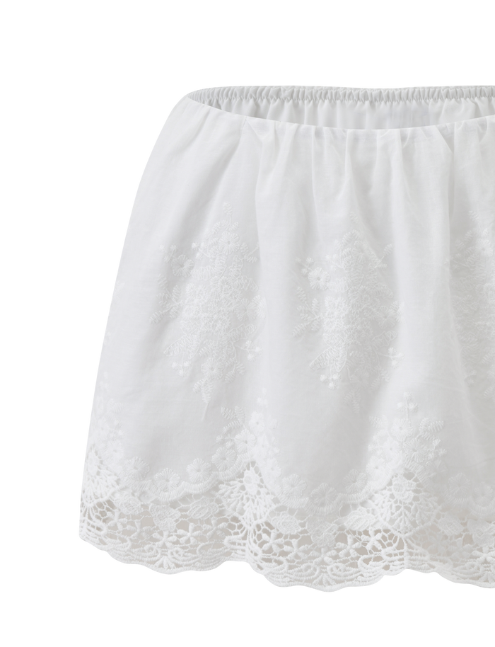 The CAILEIGH MINI SKIRT in white by TIGERMIST features an elastic waistband, delicate lace details, scalloped hem, feminine A-line fit, and intricate embroidery for a light, airy look.