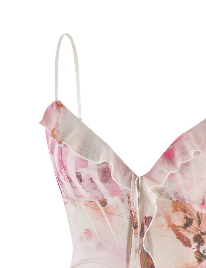A close-up of the TIGERMIST CARLY DRESS - MULTI : FLORAL reveals a light-colored, spaghetti-strap design with a watercolor-inspired pattern in pink and brown shades. The fabric has a slight sheen, while the ruffled, asymmetric neckline adds a delicate detail to the design.