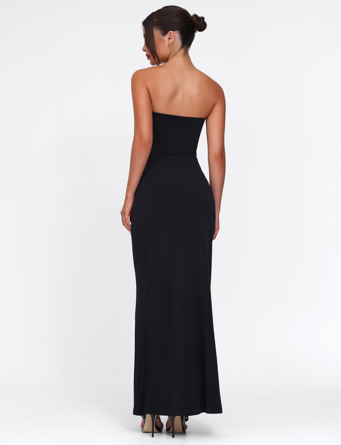 A woman with her hair in a bun is seen from behind, wearing the strapless TIGERMIST CECILY MAXI DRESS - BLACK with a sweetheart neckline and high heels, standing against a plain white background.