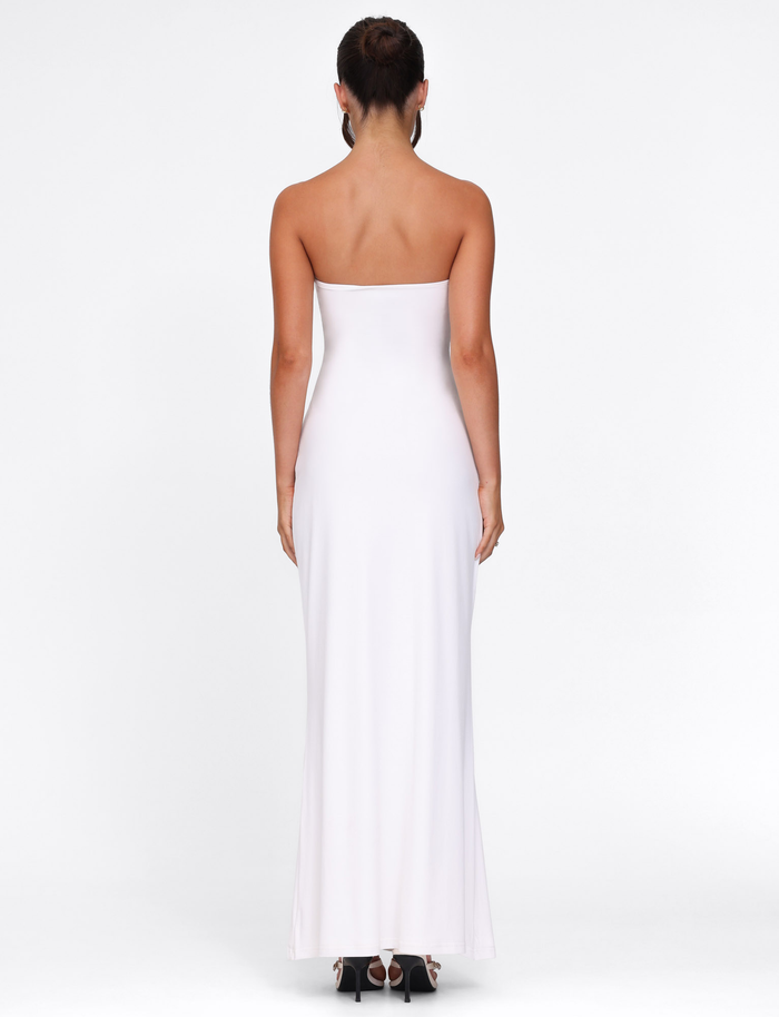 A woman faces away from the camera, modeling the TIGERMIST CECILY MAXI DRESS in white—a strapless maxi with a sweetheart neckline—paired with black open-toed heels against a plain white background.