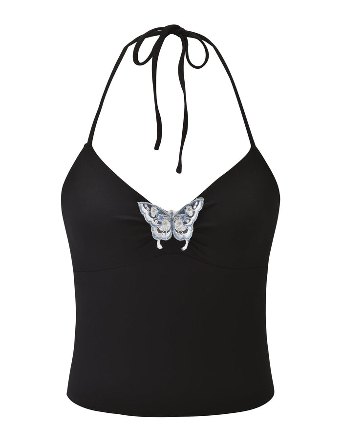 The TIGERMIST CELESTINE TOP - BLACK is a fitted halter top with a neck tie, showcasing a blue and white embroidered butterfly at the center chest.