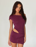 A woman wearing the COBI MINI DRESS 2.0 by TIGERMIST, featuring a glittery purple hue and an asymmetrical cut-out design, poses against a plain background.