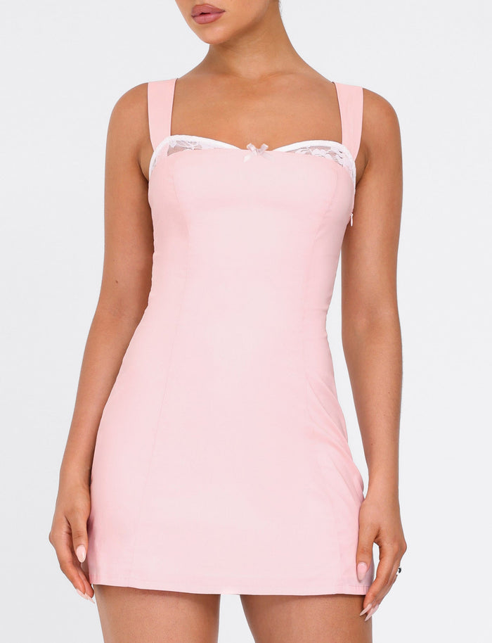 A woman wears the TIGERMIST COLSON MINI DRESS in baby pink—a sleeveless, fitted mini dress with lace trim and a bow—against a plain white background.