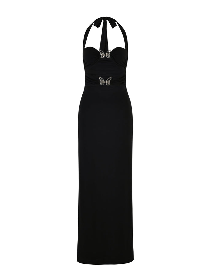 The CORALINE DRESS - BLACK by TIGERMIST is a long, elegant dress featuring a halter neckline and a form-fitting silhouette. It is adorned with two silver butterfly embellishments at the waist and chest, adding a touch of sparkle to its sleek design.