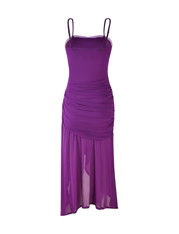 The COVE DRESS - PURPLE by TIGERMIST is a purple, sleeveless dress featuring spaghetti straps, a ruched bodice, and an asymmetrical, semi-sheer skirt that falls to mid-calf length. With its form-fitting silhouette and stylish, elegant design, this dress is set against a plain white background.