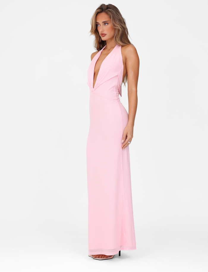 A woman poses against a white background in the TIGERMIST CRESSIDA MAXI DRESS - PINK: BABY PINK, a sleeveless, maxi-length dress with a plunging neckline and high heels. She stands slightly turned with a relaxed expression.