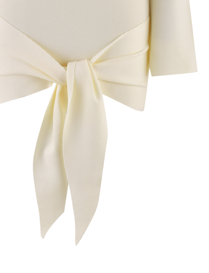 Close-up of the TIGERMIST CYPRESS DRESS in white cream, showcasing a large, neatly tied waist bow with long pointed ends. The knit fabric looks smooth with subtle texture.