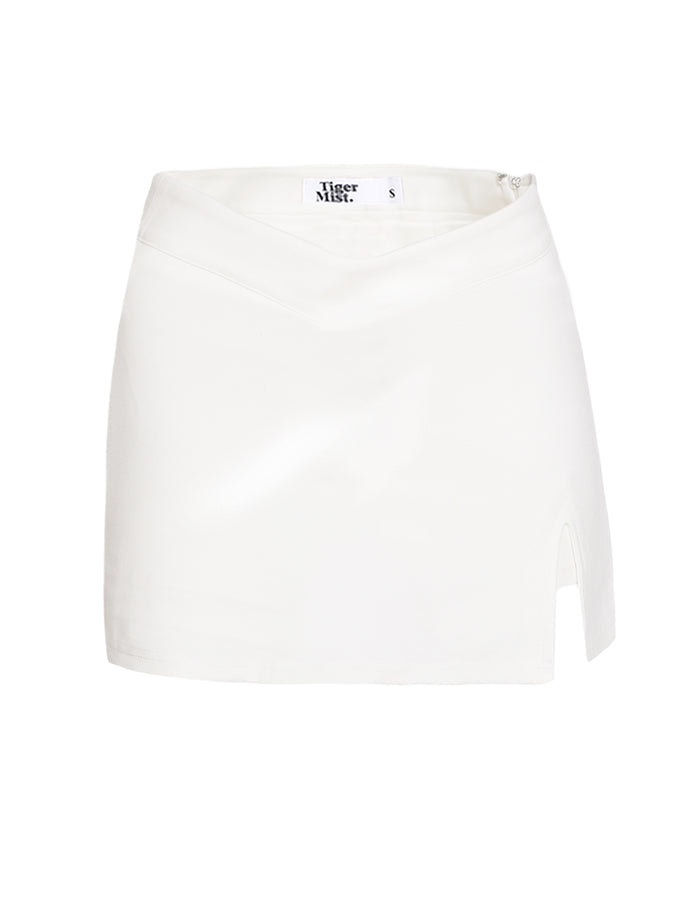 The DAPHNIE PU SKORT in white, from TIGERMIST, features a high-waisted design with a subtle drape effect at the waistband and a small slit on the left side. The tag inside reads "TIGERMIST" and indicates the size as small (S). The fabric is smooth and slightly reflective, capturing TIGERMIST's signature sleek aesthetic.