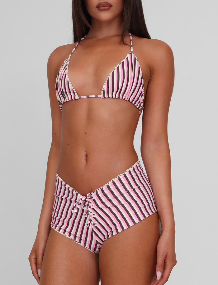 A woman models the TIGERMIST DAZZLE BIKINI BOTTOM - STRIPE, featuring pink and brown stripes with scallop lace detail on the high-waisted bottom, standing against a plain light gray background. Her face is partially out of frame.