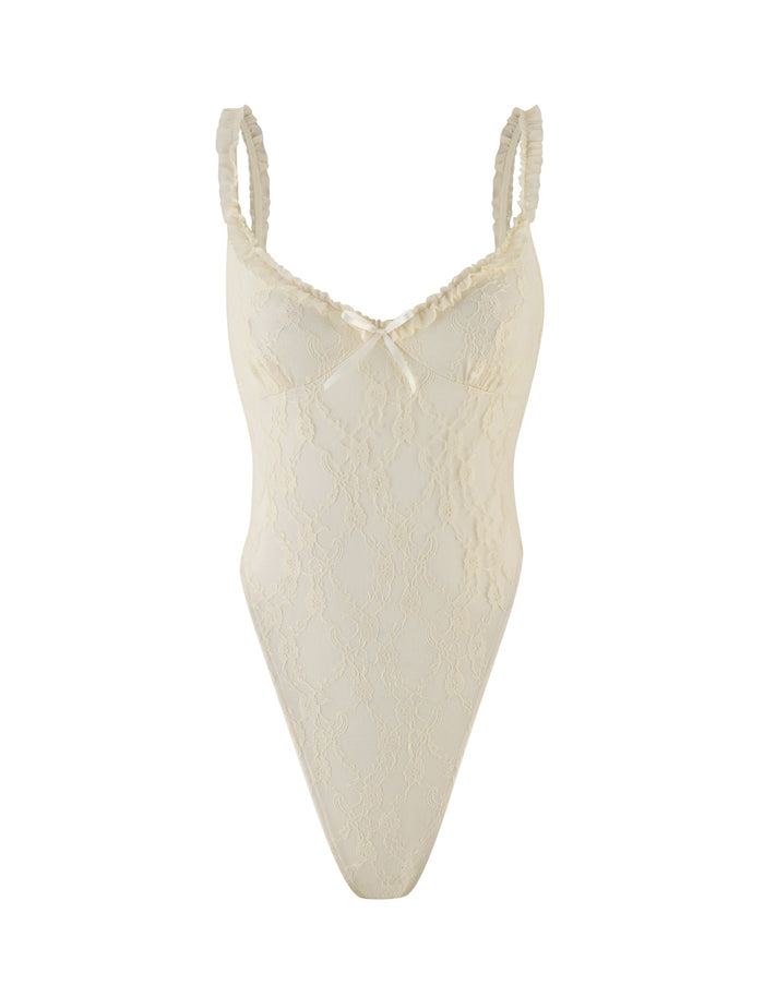 The DEJA BODYSUIT by TIGERMIST in champagne lace features ruffled mesh straps, a V-neckline, bodycon fit, and a delicate center bow.