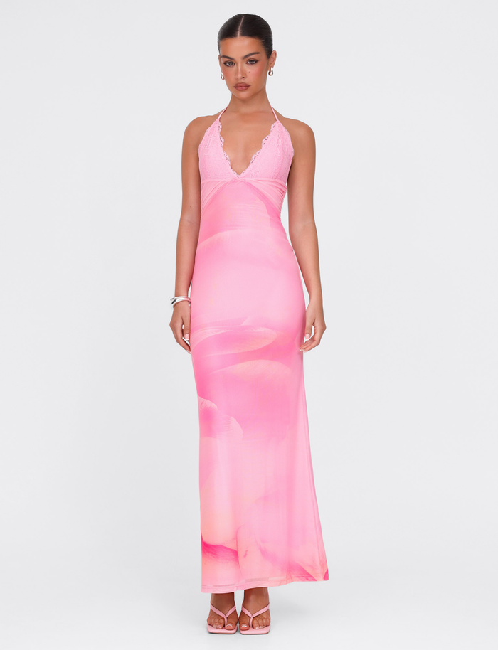 A woman stands against a white background wearing the TIGERMIST DENAE MAXI DRESS in Pink Blossom with matching heels and silver bracelets. Her hair is tied back as she looks at the camera, radiating effortless elegance.