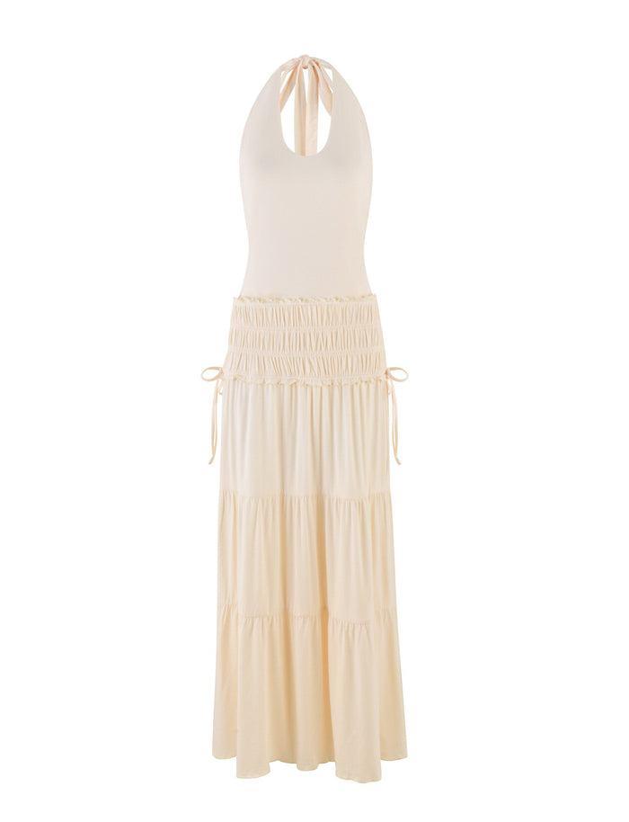 The TIGERMIST DENALI HALTER DRESS - NEUTRAL : BONE is a sleeveless, cream halter maxi dress in buttery jersey with a gathered waist, tiered skirt, and adjustable tie-back neck, shown against a white background.