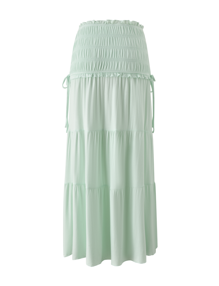 The DENALI MAXI SKIRT - SOFT MINT by TIGERMIST is a flowy modal maxi skirt with a wide shirred waistband, tiered silhouette, subtle ruffles, and side ties.