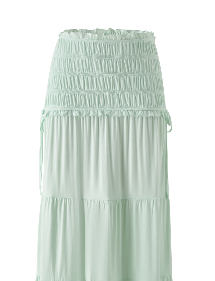 The TIGERMIST DENALI MAXI SKIRT in Soft Mint features a wide shirred elastic waistband, soft modal fabric, subtle ruffle tiers, and side drawstrings for an effortlessly flowy style.