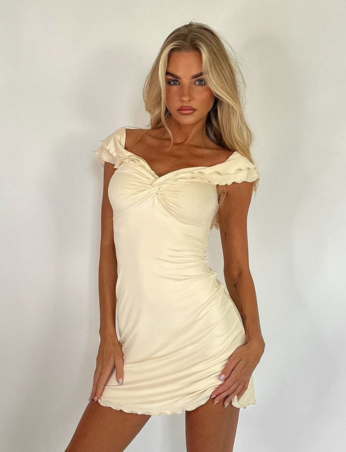 A woman with long blonde hair poses in the TIGERMIST DENALI MINI DRESS - WHITE : BONE, an off-the-shoulder, cream-colored mini dress, against a plain white background.