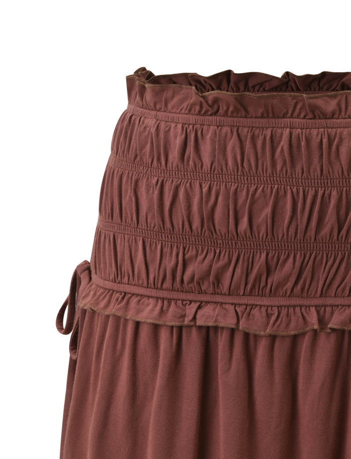 Close-up of the DENALI MINI SKIRT - CHOCOLATE by TIGERMIST, featuring a wide shirred waistband, top ruffle trim, side tie detail, and soft fabric with gentle gathers below the waist.