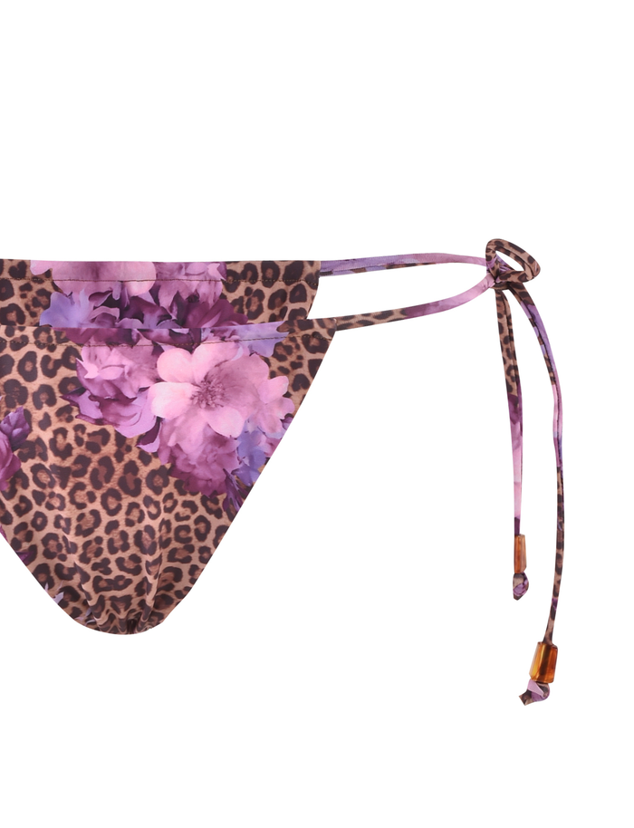 Close-up of the DESIRAE BIKINI BOTTOM by TIGERMIST in purple with a floral leopard print, showcasing adjustable side ties with wooden bead accents against a white background.