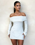 A woman with long, dark hair stands against a plain, light-colored background. She is wearing the off-the-shoulder, long-sleeved DIEDRE Jumper Dress in White : Cream from TIGERMIST. Her hair is pulled back as she looks slightly to the side with a neutral expression.