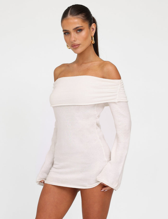 A woman with long hair tied back wears the TIGERMIST Diedre Jumper Dress in white cream. She stands against a plain white background, facing slightly to the left while looking directly at the camera. She is accessorized with large hoop earrings.