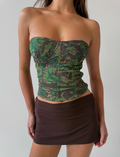 A woman models the TIGERMIST DULCE CORSET - GREEN : CAMO, a strapless camo mesh top, paired with a dark brown mini skirt against a plain light background. Her face is not shown.
