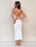 A woman with straight dark hair stands sideways, wearing the TIGERMIST EMELYN TOP in cream, styled with strappy high-heeled sandals, against a light textured wall.
