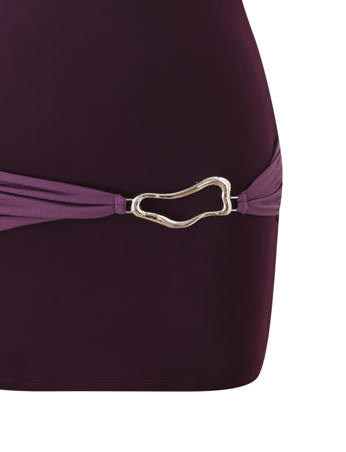 Close-up of the TIGERMIST EOS MINI DRESS in Aubergine and Iris, featuring color blocking and a gold abstract buckle at the hip. Set against a white background.