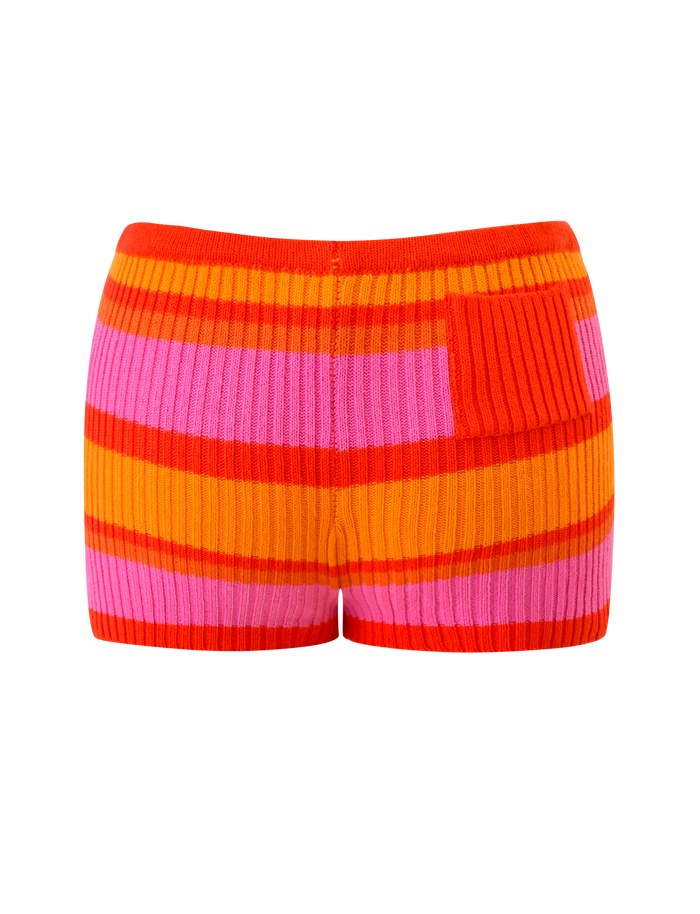 The EVERLY KNIT SHORT by TIGERMIST features high-waisted, ribbed knit fabric in sunset tropical orange, red, and pink stripes, with a small ribbed patch on the right side and an elastic waistband for a comfortable fit.