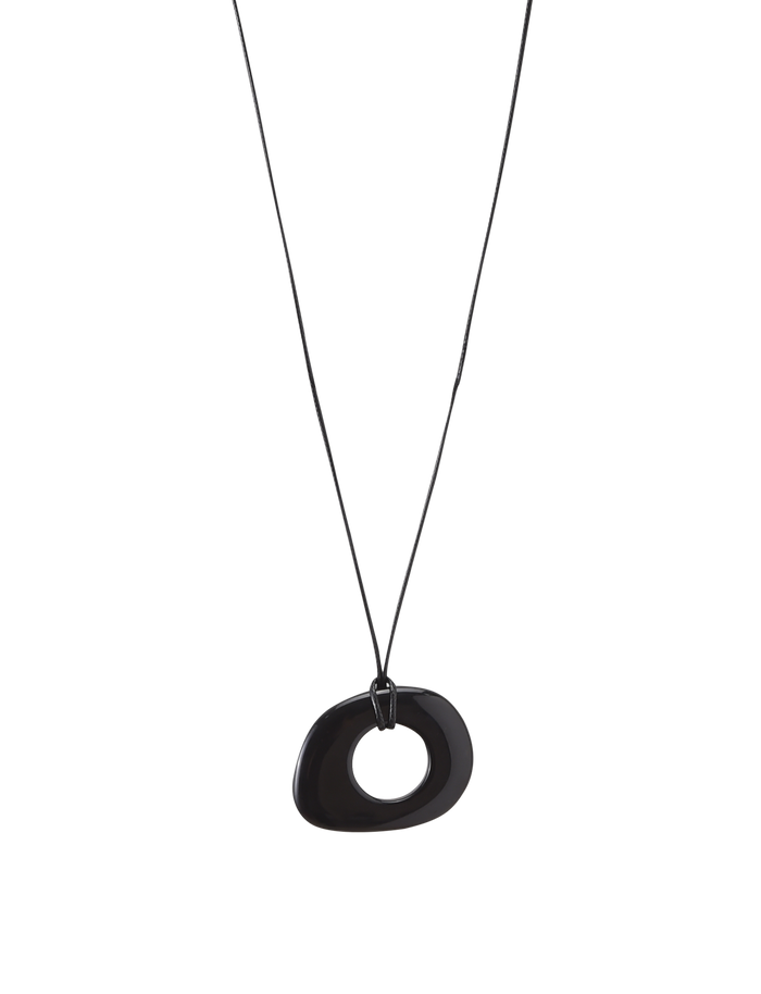 The FAELLA PENDANT NECKLACE - BLACK by TIGERMIST features a minimalist, irregular oval black resin pendant with a central hole on an adjustable cord, showcased against a plain white background.