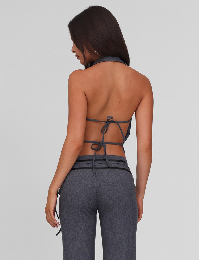 A woman with long dark hair faces away, wearing the TIGERMIST FEDRA VEST - GREY and matching high-waisted tailored pants in dark gray suiting fabric, both against a plain light background.