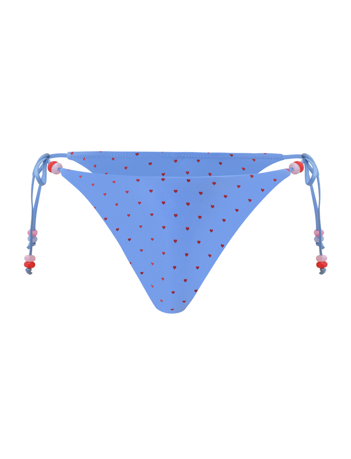 The TIGERMIST FINLEA BIKINI BOTTOM - BLUE HEART POLKA DOT features a cheeky cut, small red hearts, and adjustable side ties with red and white beads, shown on a plain white background.