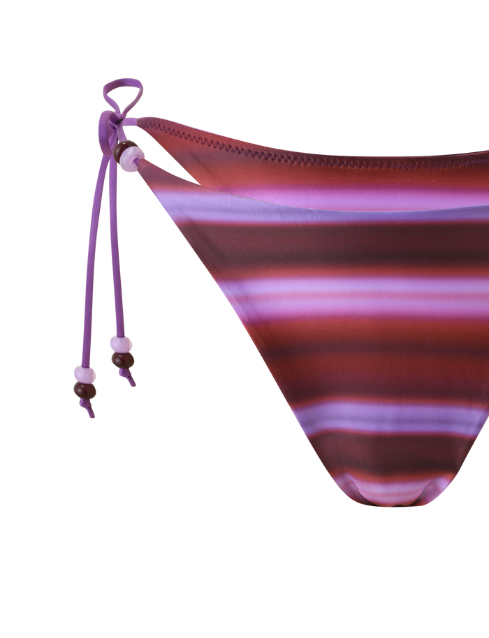 Close-up of the TIGERMIST FINLEA BIKINI BOTTOM - DUSK OMBRE STRIPE, showcasing maroon and pink horizontal stripes with ombre purple side strings featuring beaded ends, set against a white background.