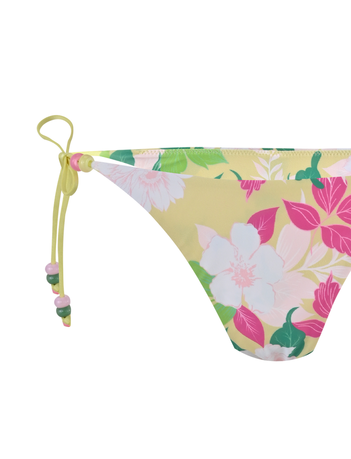 The FINLEA BIKINI BOTTOM - PAISLEY BORDER by TIGERMIST is a yellow bikini bottom with a cheeky cut, pink, green, and white paisley pattern, and side ties embellished with small beads.