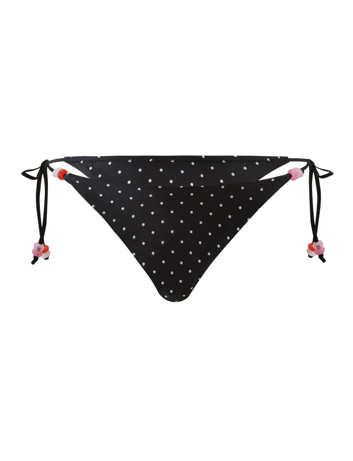 The FINLEA BIKINI BOTTOM - POLKA DOT BLACK CREAM by TIGERMIST features adjustable side ties with pink and red bead accents. This cheeky bikini bottom stands out against a plain white background.