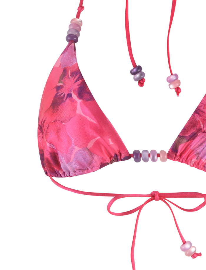 A close-up of the TIGERMIST FINLEA BIKINI TOP - PINK : HIBISCUS, showcasing its pink floral print, bead accents, halter neck, and front tied bow.