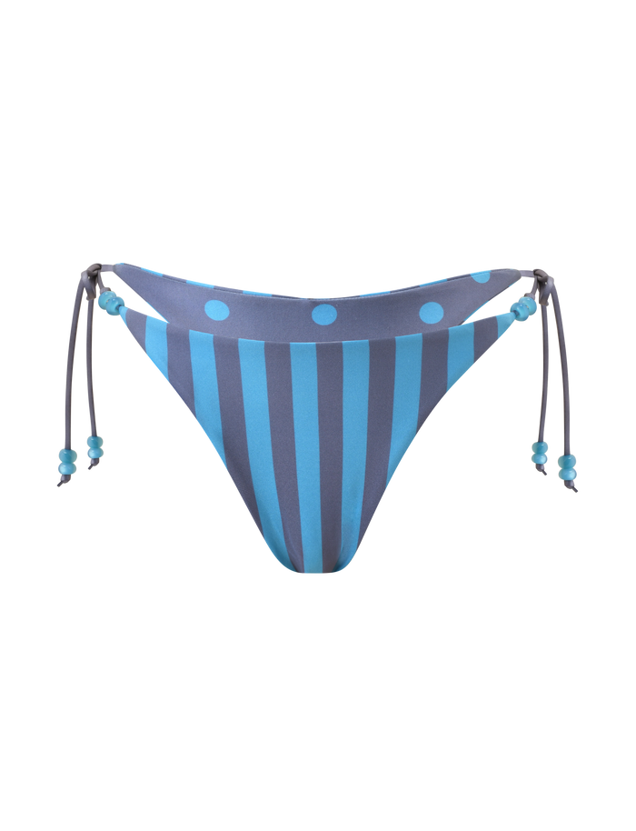 The FINLEA REVERSIBLE BIKINI BOTTOM by TIGERMIST features blue-grey vertical stripes with large polka dots at the top, a cheeky cut, and side ties with beaded details. Shown on a plain white background.