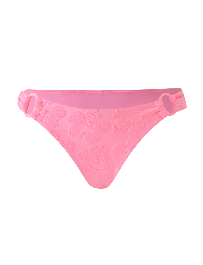 The FIORA BIKINI BOTTOM - BABY PINK by TIGERMIST features floral embossing, side ring details, a low-rise cut, and cheeky coverage, shown on a matching pink background.