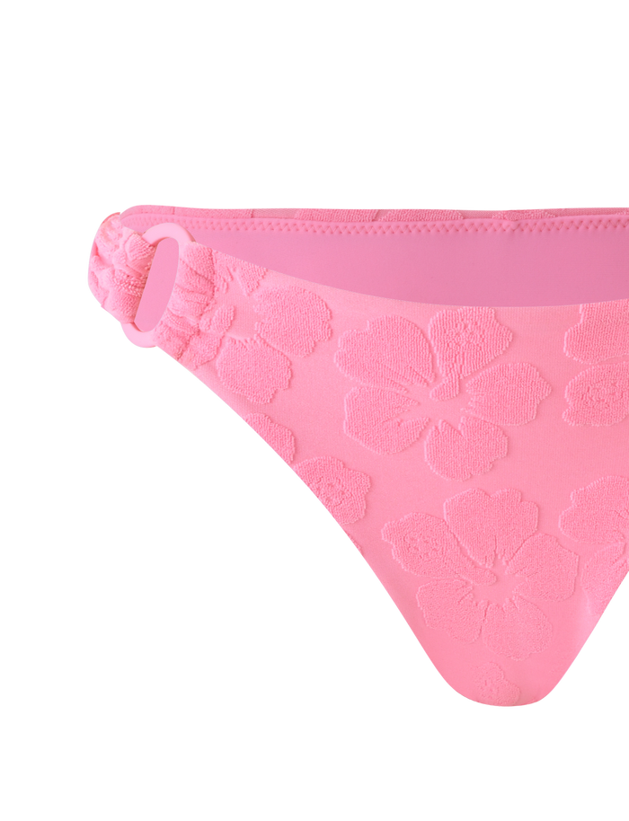 The TIGERMIST FIORA BIKINI BOTTOM in baby pink features floral embossing, a fabric-covered ring on one side, and a soft seamless waistband, shown against a matching pink background.
