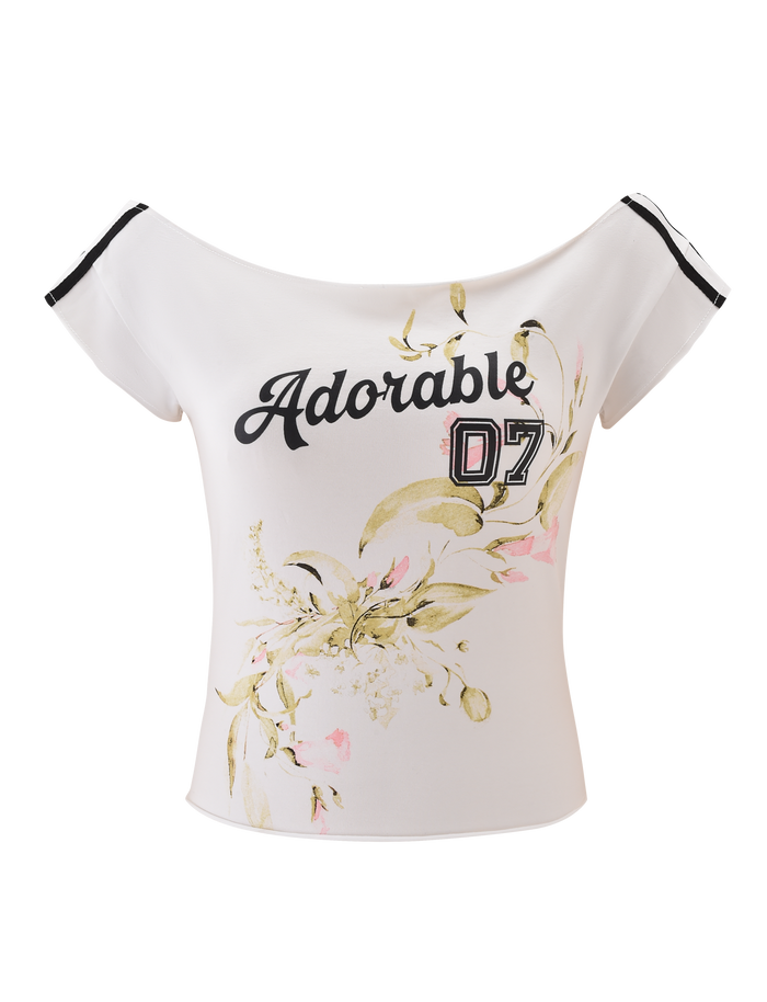 The FYNN TEE - WHITE by TIGERMIST features an off-shoulder design, black striped sleeves, “Adorable 07” on the front, and soft yellow-pink floral graphics for a playful, sporty-chic style.